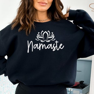 Könnte beinhalten: Schwarzer Pullover mit einer weißen Lotusblume und dem Wort "Namaste" auf der Vorderseite.