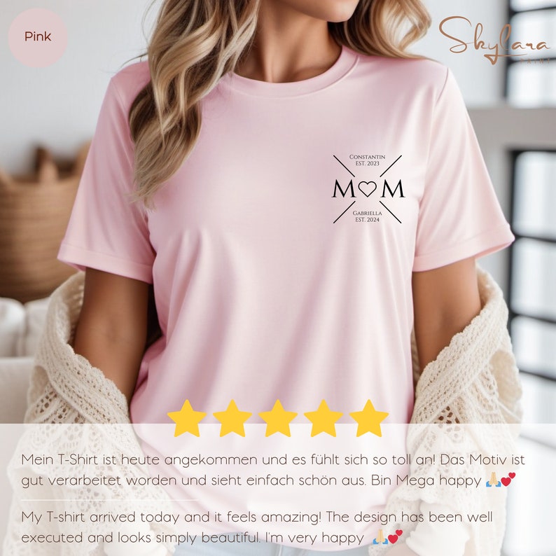 May include: Pink t-shirt with a black graphic that says "MOM" with a heart in the middle. The graphic also includes the names "Constantin" and "Gabriella" with their respective establishment years.