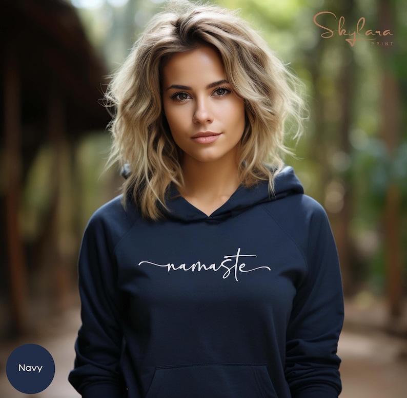 K&ouml;nnte beinhalten: Ein marineblauer Hoodie mit einem wei&szlig;en "namaste"-Aufdruck. Der Hoodie hat eine Kapuze mit Kordelzug und eine K&auml;ngurutasche.