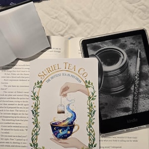 Peut inclure: Une carte décorative pour Suriel Tea Co. présente une illustration fantaisiste d'une tasse à thé remplie d'un motif de galaxie, avec un sachet de thé qui y est plongé. La carte est entourée d'une bordure de vigne verte.