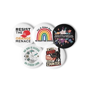Puede incluir: Cinco chapas redondas con diversos diseños políticos. Una chapa blanca dice RESIST THE ORANGE MENACE con un sombrero rojo. Otra chapa blanca muestra un arcoíris. Una chapa negra presenta motivos florales. Dos chapas blancas muestran una luna creciente con un puño y un gato negro con texto.