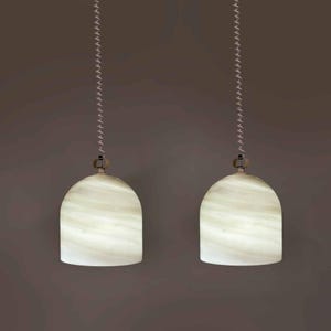 Può includere: Due lampade a sospensione dall'aspetto bianco marmorizzato. Ogni lampada è appesa a una catena argentata e ha una forma arrotondata a campana. Lo sfondo è marrone tenue.