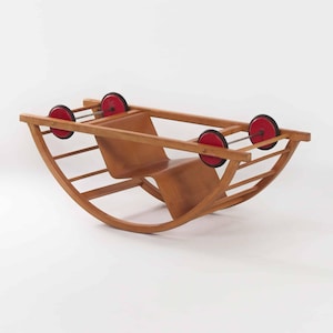 Könnte beinhalten: Ein hellbrauner Holzschaukelstuhl mit Sitz und Rückenlehne. Der Stuhl hat vier rote Räder am Rahmen befestigt. Das Design ist schlicht und modern. Geeignet für ein Kinderzimmer oder Spielzimmer. Abmessungen in Zentimetern.