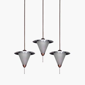 Può includere: Tre luci a sospensione argentate e bianche con un paralume a forma di cono appeso a cavi marroni.