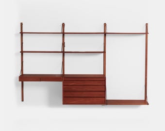 May include: A mid-century modern wall unit in a warm reddish-brown wood tone. The unit features shelves, a desk, drawers, and a hanging rod. The design is modular, with adjustable components and leather straps for support.