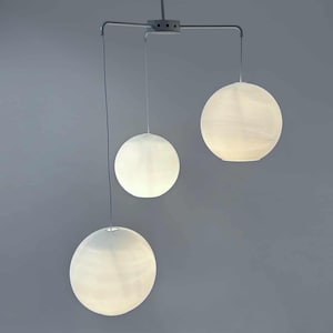Può includere: Un lampadario moderno a tre luci con paralumi bianchi a forma di sfera. I paralumi sono sospesi da una struttura in metallo argentato.