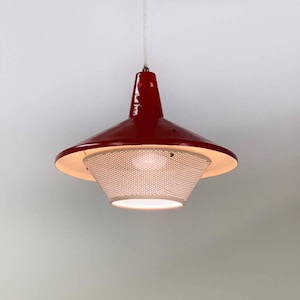 Può includere: Una lampada a sospensione rossa e bianca con un paralume in metallo perforato. La luce è sospesa da un cavo bianco.