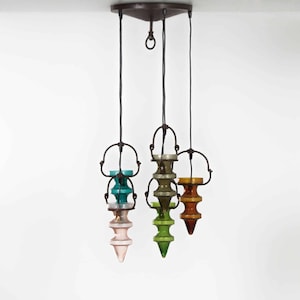 Può includere: Un lampadario a più livelli con una struttura in metallo nero e cinque paralumi in vetro di diversi colori, tra cui rosa, verde, blu e marrone.