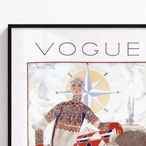 Op de afbeelding: Een ingelijste vintage Vogue tijdschriftomslag met een illustratie van een persoon in een trui met patroon en een bril voor een kompasroos en een voertuig. Het woord VOGUE staat bovenaan in zwarte hoofdletters gedrukt.