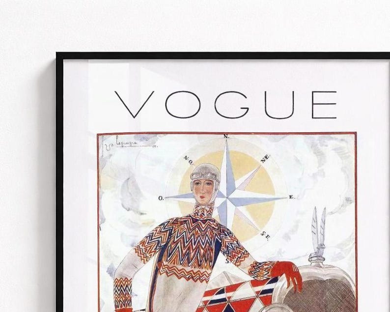 Op de afbeelding: Een ingelijste vintage Vogue tijdschriftomslag met een illustratie van een persoon in een trui met patroon en een bril voor een kompasroos en een voertuig. Het woord VOGUE staat bovenaan in zwarte hoofdletters gedrukt.