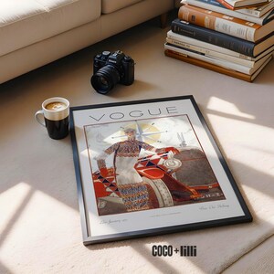 Op de afbeelding: Een ingelijste vintage Vogue tijdschriftomslag met een illustratie van een persoon in een trui en rok met patroon, staand naast een auto. Het kunstwerk bevat de tekst VOGUE bovenaan en decoratieve geometrische elementen in rood, blauw en wit.