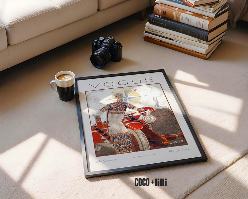Op de afbeelding: Een ingelijste vintage Vogue tijdschriftomslag met een illustratie van een persoon in een trui en rok met patroon, staand naast een auto. Het kunstwerk bevat de tekst VOGUE bovenaan en decoratieve geometrische elementen in rood, blauw en wit.