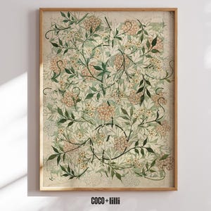 May include: A rectangular wall art print in a wooden frame featuring a botanical pattern of light green leaves and clusters of small, pale orange flowers on a cream background. The text COCO + lilli is printed in black at the bottom center.