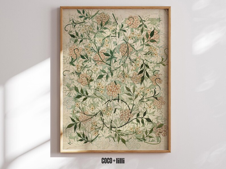 May include: A rectangular wall art print in a wooden frame featuring a botanical pattern of light green leaves and clusters of small, pale orange flowers on a cream background. The text COCO + lilli is printed in black at the bottom center.