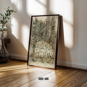 May include: A rectangular framed wall art piece featuring a botanical print with intricate green leaves, thin brown stems, and soft pink floral clusters on a light beige background. The text COCO + lilli is printed in black at the bottom center.