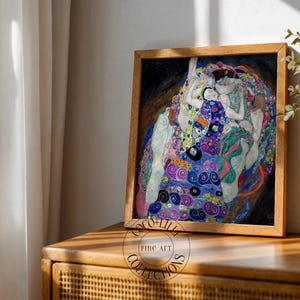 May include: A framed art print featuring a reproduction of Gustav Klimt's The Virgin, displaying multiple figures in a swirling composition of blue, purple, green, and gold patterns, enclosed in a light-toned wooden frame with a circular logo.