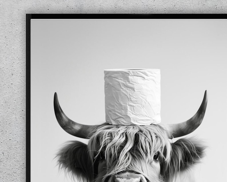 May include: Black and white print of a Highland cow with a roll of white toilet paper balanced on its horns. The cow has long, shaggy fur and curved horns. The image is framed in a black border.