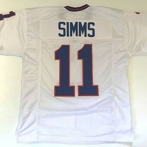 May include: White football jersey with blue and red trim. The number "11" and the name "SIMMS" are printed on the back in blue with a red outline.