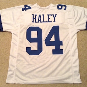 May include: White football jersey with blue numbers and lettering. The jersey has the number "94" and the name "HALEY" on the back.