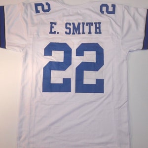 May include: White football jersey with blue and black stripes on the sleeves. The number 22 is printed on the back in blue with the name "E. SMITH" above it.