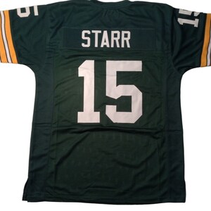 May include: Green football jersey with white lettering. The jersey has the name "STARR" and the number "15" on the back.