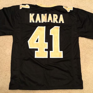 May include: Black football jersey with gold lettering. The name "KAMARA" and the number "41" are on the back of the jersey.