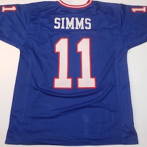 May include: A blue football jersey with white numbers and the name "SIMMS" on the back. The jersey has red and white trim on the sleeves and collar.