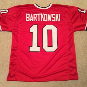 May include: Red football jersey with white lettering. The name "BARTKOWSKI" and the number "10" are on the back of the jersey.
