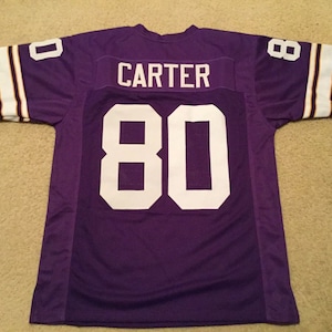 May include: Purple football jersey with white lettering. The name "CARTER" and the number "80" are on the back of the jersey.