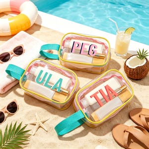 May include: Three clear cosmetic bags with colorful accents and handles, each with a different name in bold letters: "PEG", "ULA", and "TIA". The bags are filled with beauty products and are set on a sandy beach with sunglasses, a drink, and a coconut.