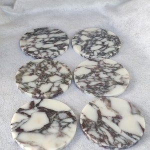 Pu&ograve; includere: Sei sottobicchieri rotondi in marmo con sfondo bianco e un motivo a spirale di venature viola scuro e grigie.