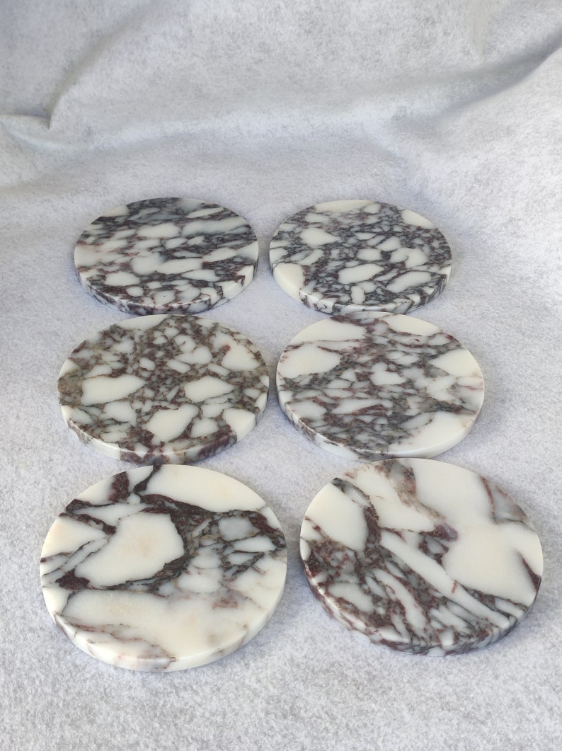 Pu&ograve; includere: Sei sottobicchieri rotondi in marmo con sfondo bianco e un motivo a spirale di venature viola scuro e grigie.