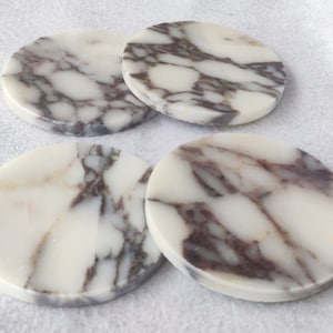 Pu&ograve; includere: Quattro sottobicchieri rotondi in marmo bianco con venature marroni. I sottobicchieri sono lisci e lucidi.