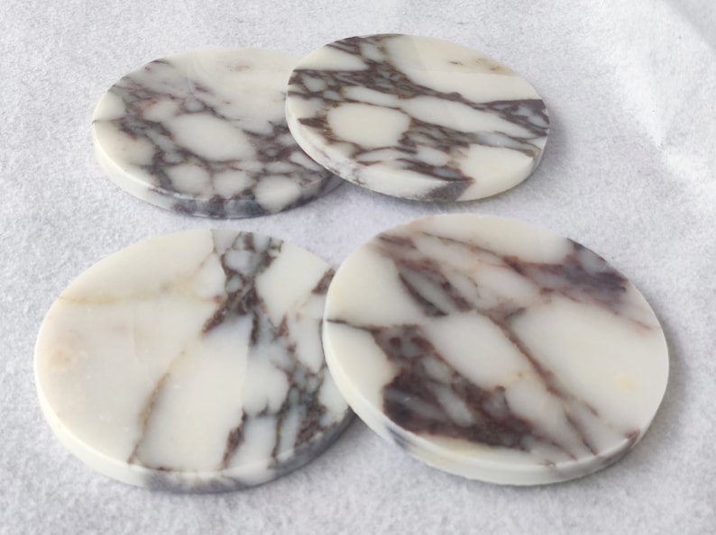 Pu&ograve; includere: Quattro sottobicchieri rotondi in marmo bianco con venature marroni. I sottobicchieri sono lisci e lucidi.