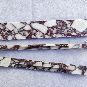 Puede incluir: Tres objetos con un patrón de mármol en blanco y burdeos. El más grande es rectangular con extremos redondeados, los otros son largos y estrechos. Los objetos tienen un acabado pulido y se muestran sobre una superficie blanca. Probablemente decorativos.