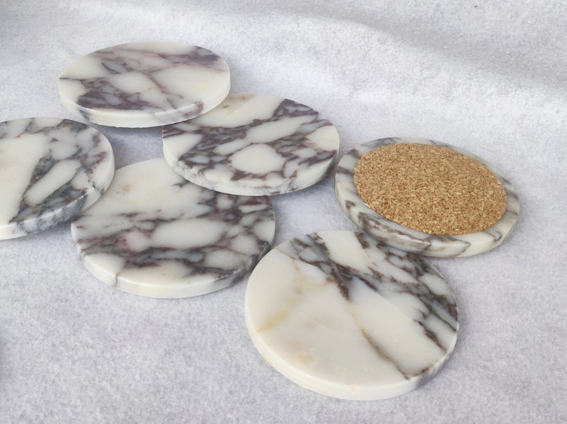 Pu&ograve; includere: Set di sei sottobicchieri rotondi in marmo con un motivo a marmo bianco e grigio. Un sottobicchiere ha un inserto in sughero.