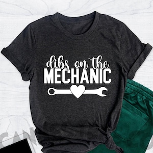 Może przedstawiać: Szary t-shirt w kolorze ciemnego melanżu z napisem "dibs on the mechanic" w białym kolorze. Pod napisem znajduje się biały klucz z sercem w środku.