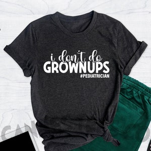 May include: A dark heather grey t-shirt with white text that reads "i don't do grown ups #pediatrician".