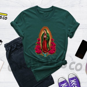 May include: A dark green t-shirt with a graphic print of Our Lady of Guadalupe, a religious figure, surrounded by red roses.
