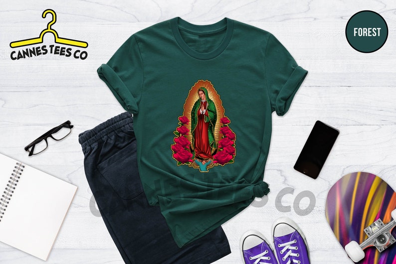 May include: A dark green t-shirt with a graphic print of Our Lady of Guadalupe, a religious figure, surrounded by red roses.