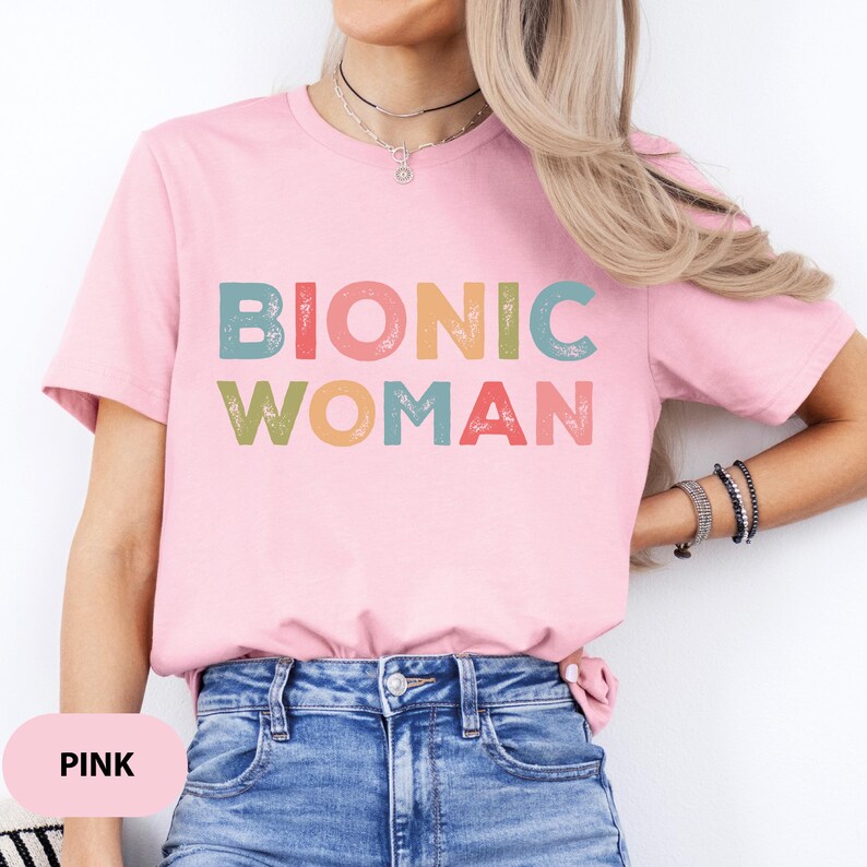May include: Pink t-shirt with the text "Bionic Woman" in colorful, distressed lettering.
