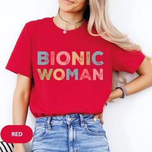 May include: Red t-shirt with the text "BIONIC WOMAN" in colorful, distressed lettering.