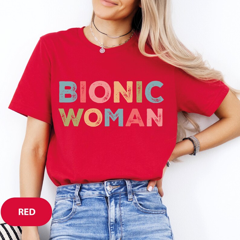 May include: Red t-shirt with the text "BIONIC WOMAN" in colorful, distressed lettering.