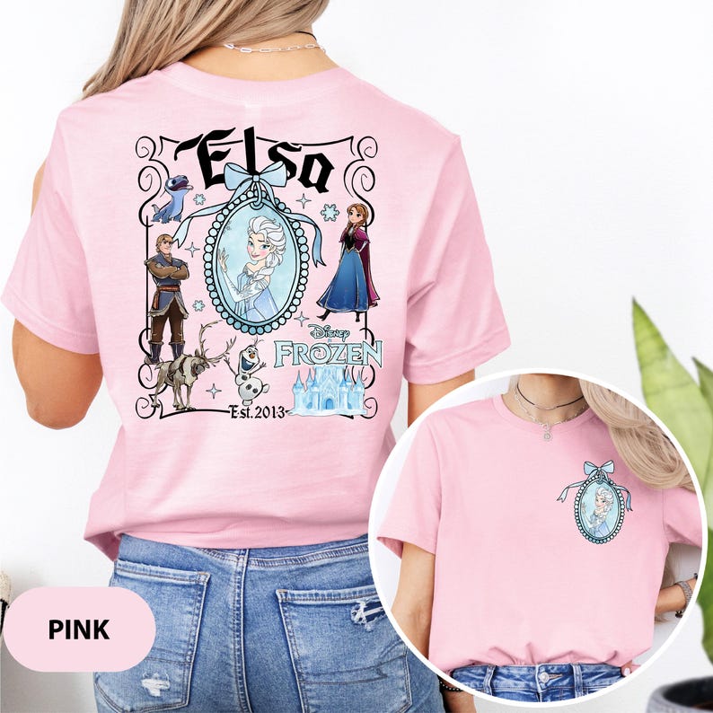 May include: Pink t-shirt featuring a Disney Frozen design. The back of the shirt displays the name "Elsa" above a framed image of Elsa, with other characters and the text "Frozen" and "Est. 2013". A smaller version of the design is on the front.
