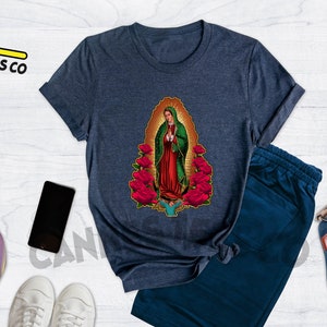May include: A navy blue t-shirt with a graphic of Our Lady of Guadalupe surrounded by red roses. The t-shirt is made of a soft, comfortable material and has a crew neck.