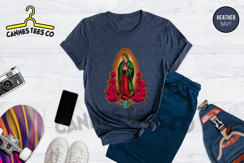 May include: A navy blue t-shirt with a graphic of Our Lady of Guadalupe surrounded by red roses. The t-shirt is made of a soft, comfortable material and has a crew neck.