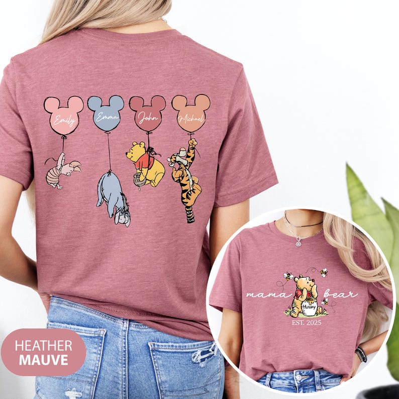 May include: A heather mauve t-shirt with a Winnie the Pooh theme. The back of the shirt features four Mickey Mouse balloons with names written on them. Each balloon is attached to a different Winnie the Pooh character. The front of the shirt features a Winnie the Pooh character with the text "mama bear est. 2025".