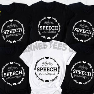 Op de afbeelding: Vijf T-shirts in zwart en wit met een cirkelvormig ontwerp met de tekst "SPEECH pathologist" en een handgebaar voor de letter "S". De tekst "compassionate, caring, dedicated, reliable, loyal, kind" omringt de cirkel.