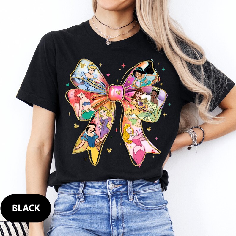 May include: Black t-shirt featuring a colourful bow design with Disney princesses. The bow is made up of different princesses, including Cinderella, Ariel, Belle, and Rapunzel.