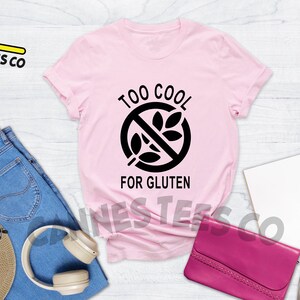 May include: Pink t-shirt with a black graphic that says "Too Cool For Gluten" and a crossed-out wheat symbol.